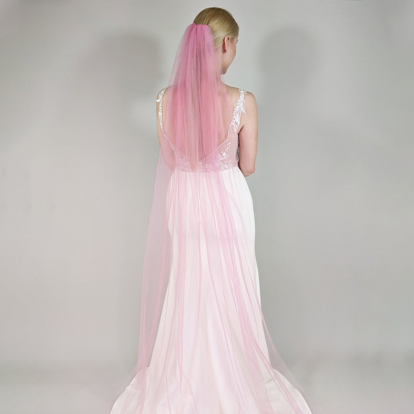 Woman wearing a pink wedding veil against a plain background