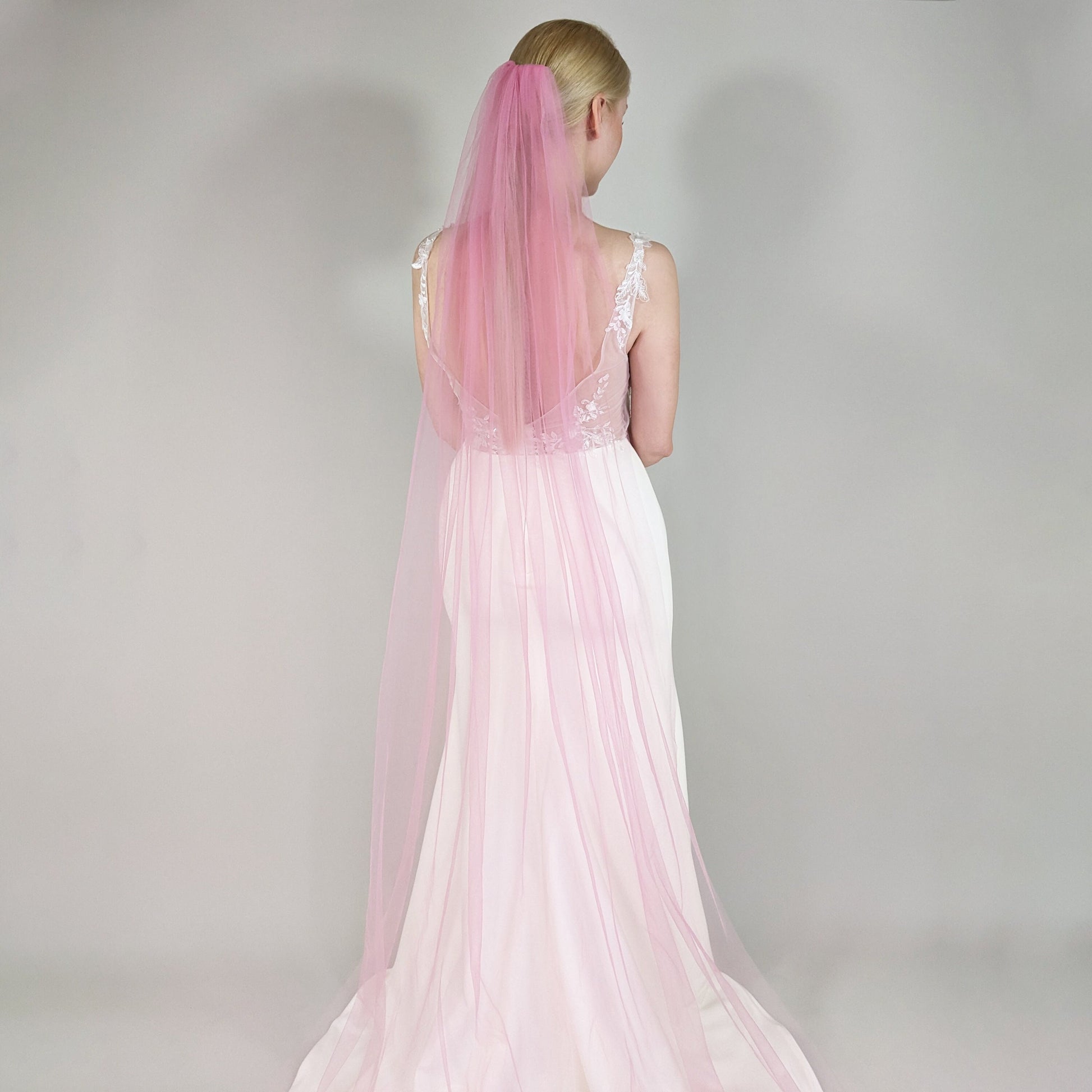 Woman wearing a pink wedding veil against a plain background