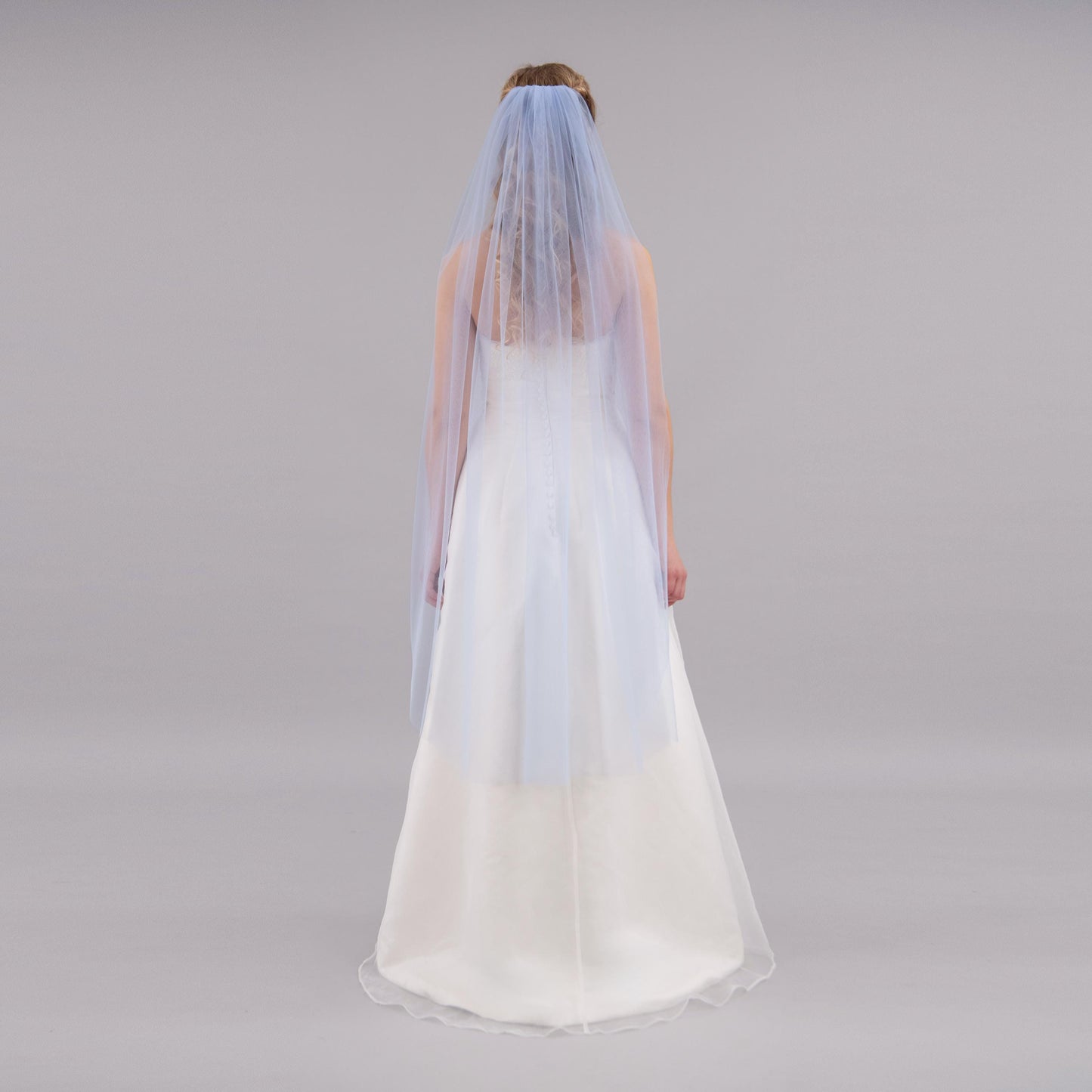 Person wearing a white wedding dress with a blue veil on a gray background