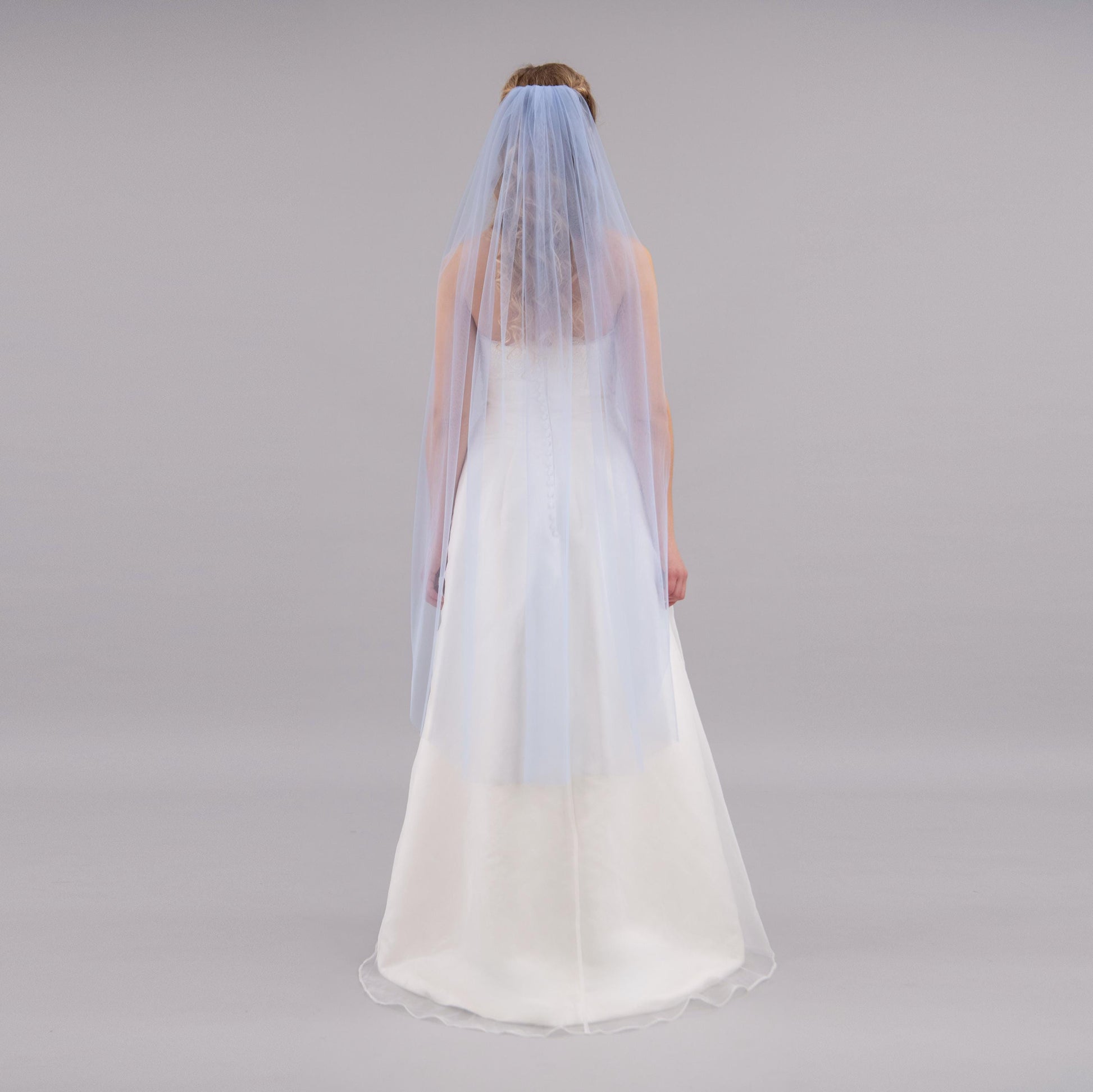 Person wearing a white wedding dress with a blue veil on a gray background