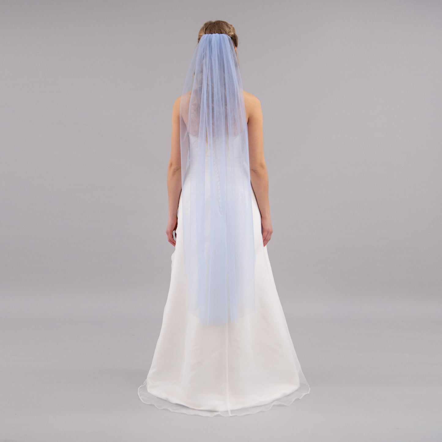 Woman wearing a white wedding dress with a blue veil on a gray background