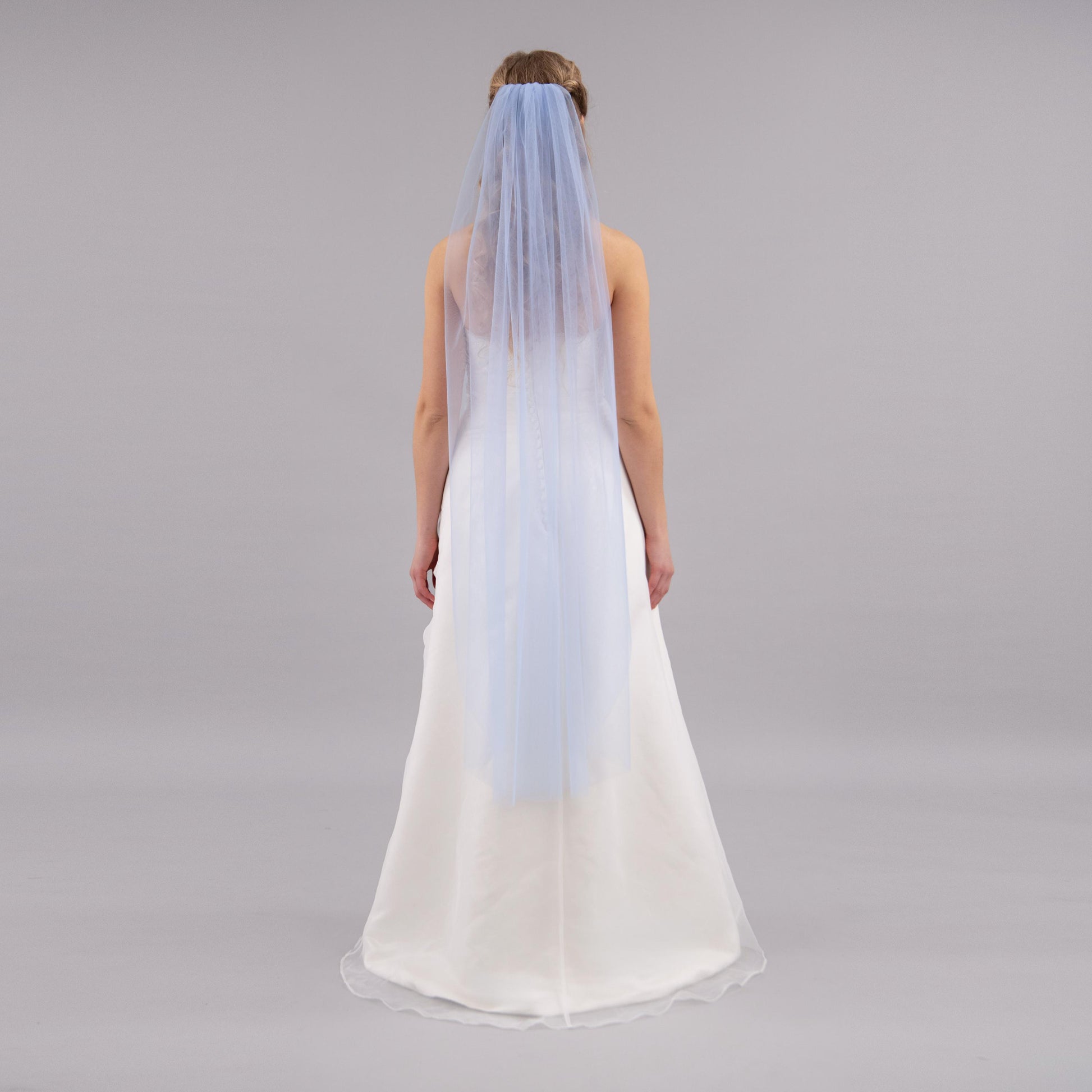 Woman wearing a white wedding dress with a blue veil on a gray background