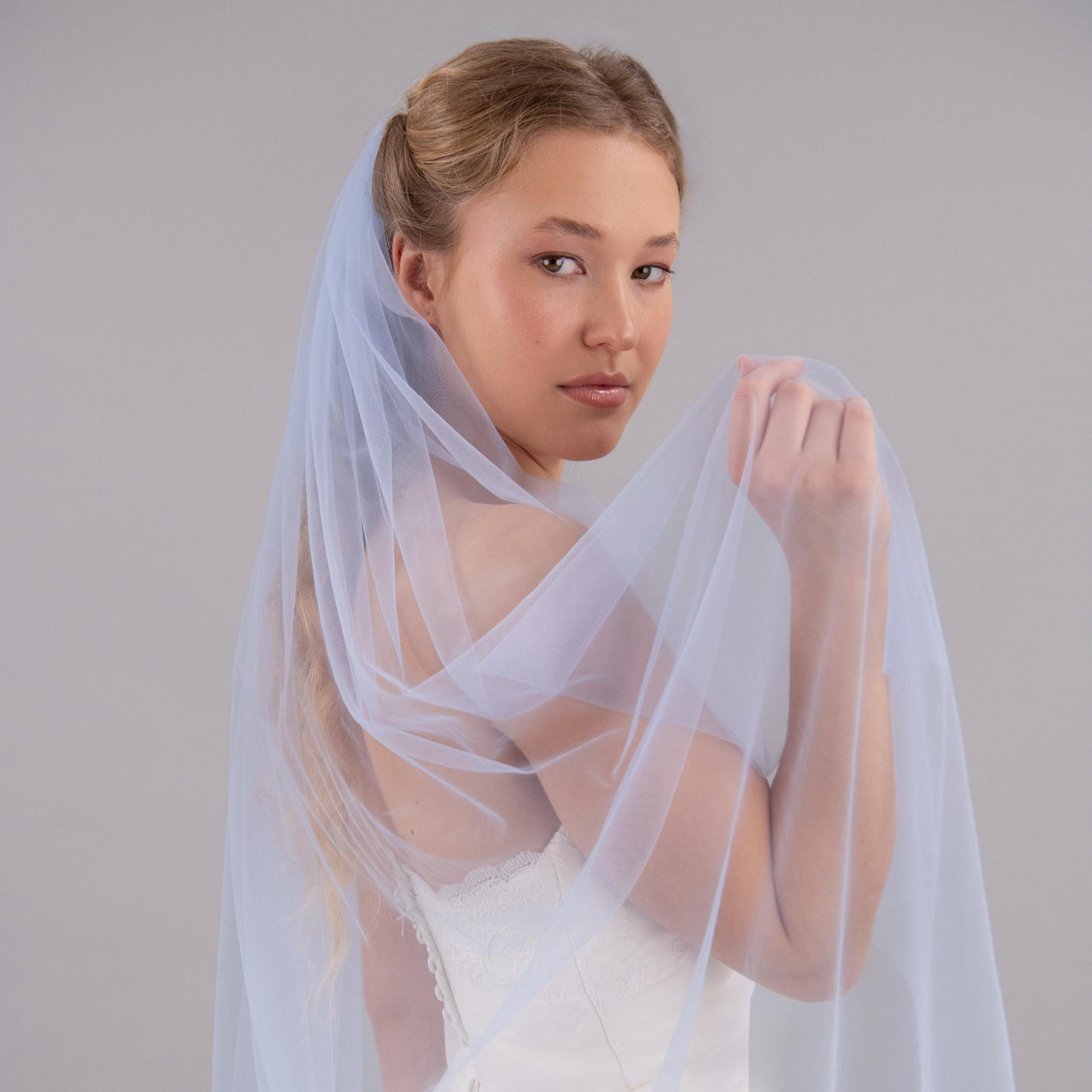 Woman wearing a light blue wedding veil against a gray background