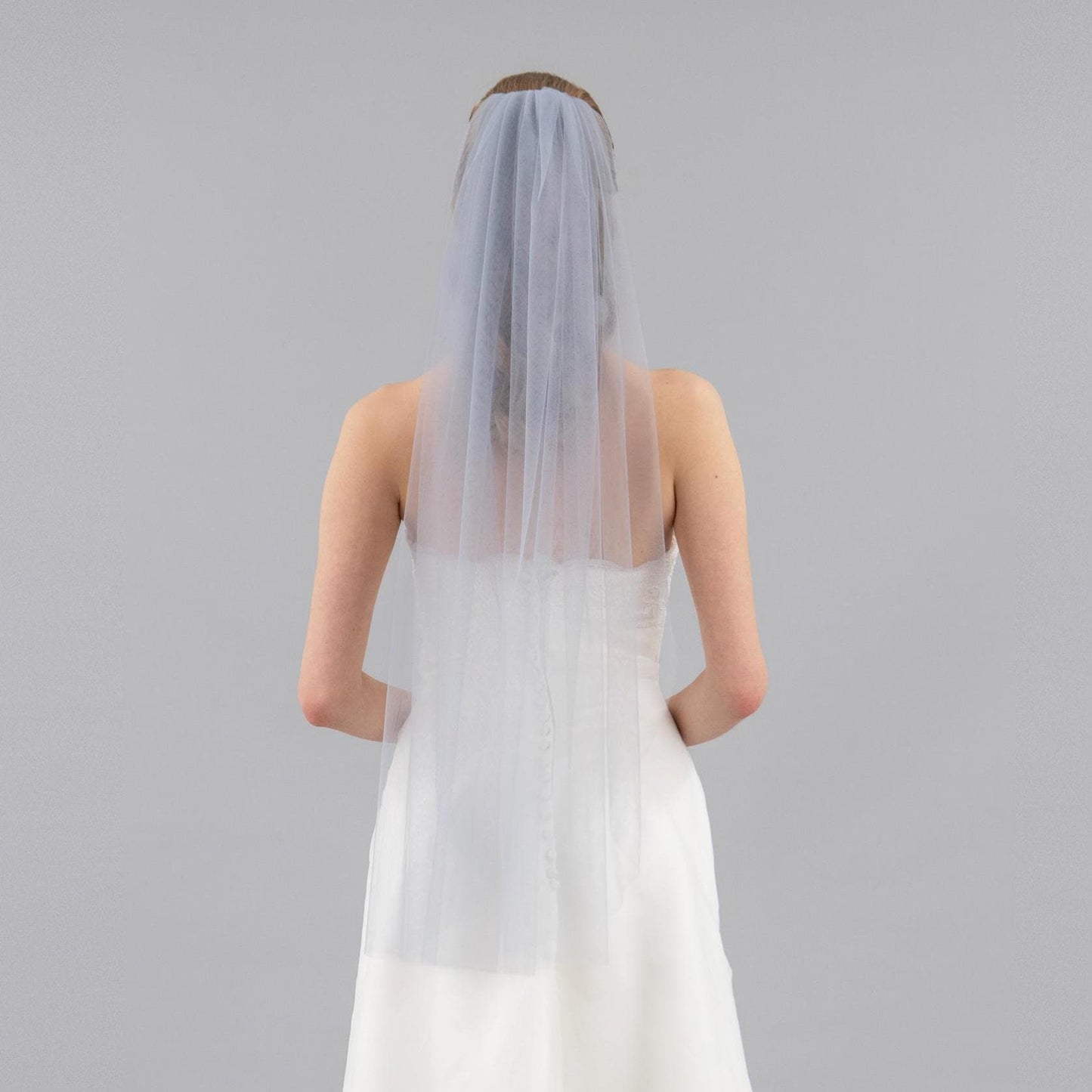 Person wearing a white wedding dress with a sheer gray veil on a gray background