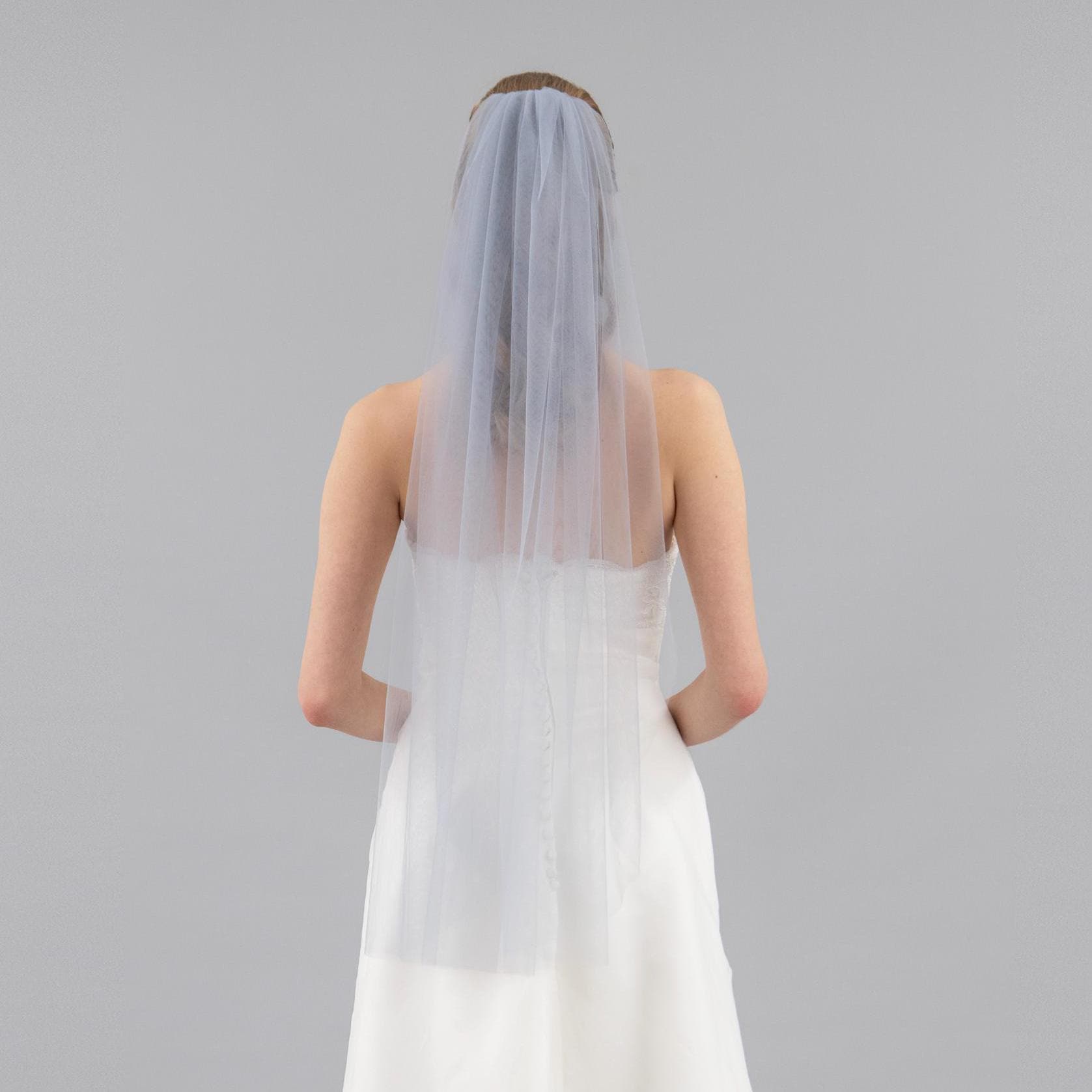 Person wearing a white wedding dress with a sheer gray veil on a gray background