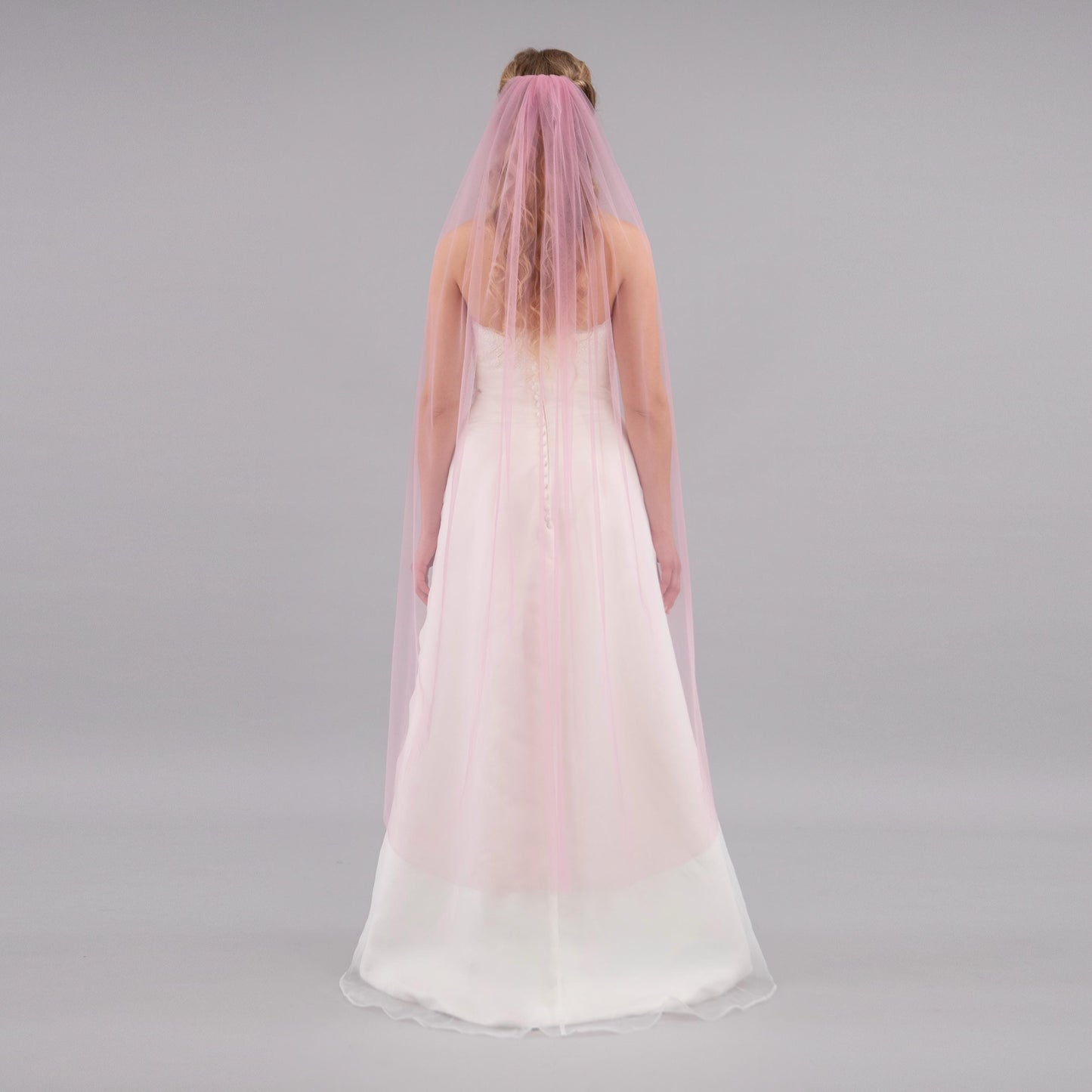 Woman wearing a long, light pink veil on a gray background