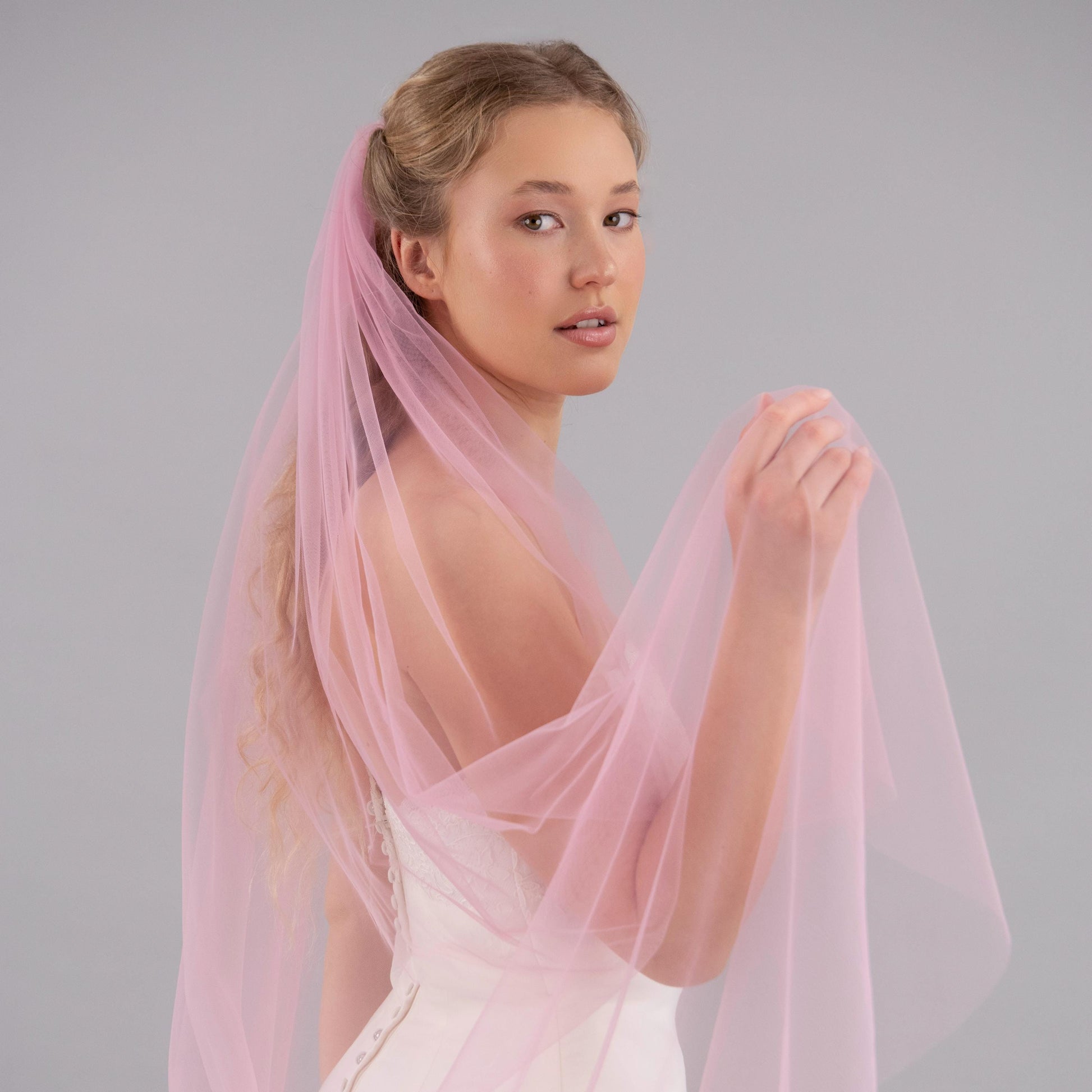 Woman wearing a light pink veil against a gray background
