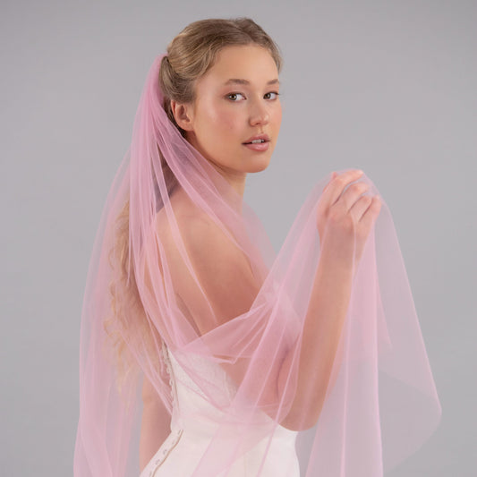 Woman wearing a light pink veil against a gray background
