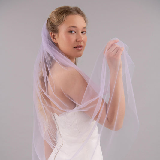 Woman wearing a white wedding dress with a light purple veil against a plain background