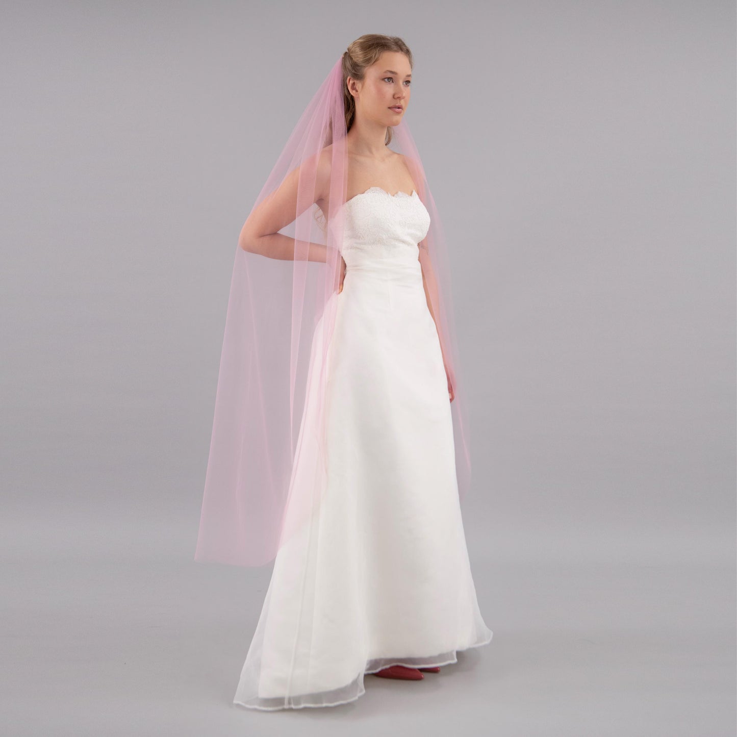 Woman wearing a white strapless wedding dress with a pink veil on a gray background