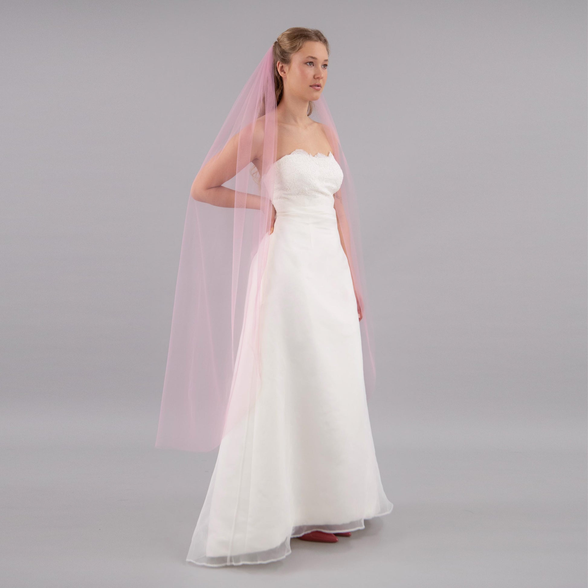 Woman wearing a white strapless wedding dress with a pink veil on a gray background